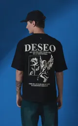 Remera de manga corta y cuello redondo con calce oversize. Presenta una estampa frontal en color crema con diseño artístico de un ángel y una rosa, acompañada de frases en español. Confeccionada en algodón premium.