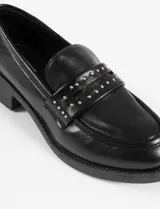 Mocasines negros de cuero vegano con suela gruesa y tira superior decorada con tachas metálicas doradas.