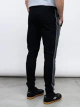 Pantalón deportivo Umbro modelo UNY, color gris melange, confeccionado en tejido de piqué. Presenta puños ajustados en los tobillos, cordón de ajuste en la cintura y una franja lateral gris claro con ribete blanco. El logo Umbro está bordado en la pierna izquierda.