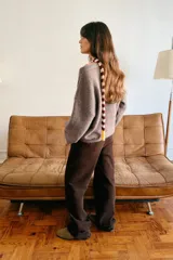 Jersey de punto color marrón topo, con cuello drapeado decorado con un broche metálico dorado y mangas largas de corte holgado.