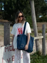 Bolso tote de denim azul oscuro con asas de hombro y detalle de bordado circular con texto en el frente.