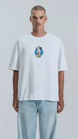 Remera blanca de manga corta con cuello redondo y calce oversize. Presenta un estampado central pequeño de Mickey Mouse vestido de chef sobre un círculo azul.