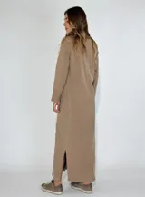 Vestido largo tipo camisero color beige, con botones frontales, cuello camisero, mangas largas con puños abotonados y bolsillos en el pecho.