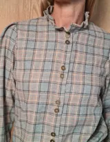 Camisa de manga larga con estampado de rayas verticales en tonos blanco y lila. Presenta cuello alto con volados, cierre frontal con doble botonadura y puños con volados.