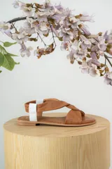 Sandalias chatitas de cuero color suela, con diseño de tiras cruzadas en el empeine y detalle de tira elástica blanca en el talón.
