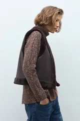 Chaleco reversible de corte recto, con un lado de cuero sintético color chocolate y el otro lado de piel sintética al tono. Presenta cuello redondo y diseño sin mangas.