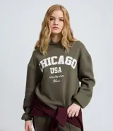 Buzo con capucha de algodón afelpado, color gris topo, con estampado frontal de letras blancas estilo universitario. Presenta mangas largas con puños acanalados y ruedo también acanalado.