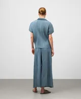 Camisa de poliéster reciclado color gris azul con textura crinkle. Presenta cuello solapa, manga corta redondeada y botonadura frontal oculta.