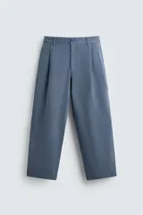 Pantalón de hombre color azul grisáceo, estilo balloon fit, confeccionado en mezcla de algodón y lino. Presenta pliegues en el delantero, cierre frontal con botón y cremallera, bolsillos laterales y bolsillos traseros de plastrón.