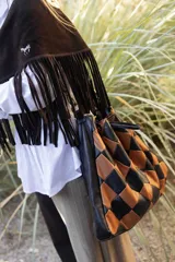 Bolso de hombro tipo hobo con diseño de rombos entrelazados en cuero negro y marrón. Presenta una silueta amplia y flexible con detalles de flecos largos en la parte superior.