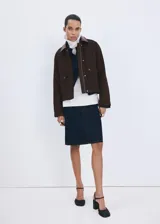 Chaqueta de algodón estilo tejano de corte recto, color marrón, con cuello camisero de efecto piel en contraste, manga larga y dos bolsillos de parche con solapa y botón en el frente. Cuenta con cierre oculto de cremallera y botones.
