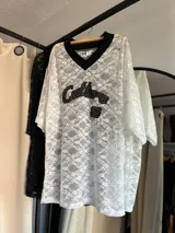 Remerón de encaje negro con diseño de cuello en V y mangas cortas. Presenta un estampado frontal bordado con texto y el número 32.