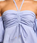 Blusa de tricolina color celeste, con diseño hombro a hombro, escote halter, fruncido en el pecho con lazo ajustable, y mangas abullonadas cortas.