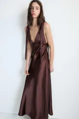 Vestido midi satinado color marrón, con escote en V y tirantes anchos ajustables con lazada en los hombros. Presenta cierre lateral con cremallera oculta.