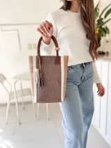 Bolso matero de cuero color taupe con textura croco y detalles en cuero color marrón. Tiene doble asa de mano y un dije de borla.