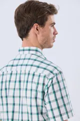Camisa de manga corta a cuadros en tonos blanco, azul y gris, con cuello abotonado, bolsillo en el pecho y cierre frontal con botones.