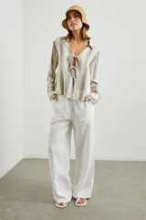 Blusa de lino a rayas verticales de color blanco, naranja, verde y marrón, con cuello camisero, mangas largas con puños y lazos ajustables en el escote.