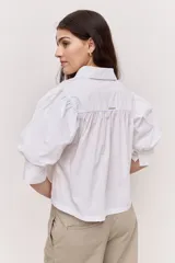 Camisa azul marino de cuello clásico, mangas abullonadas a tres cuartos y detalle fruncido en el frente. Presenta una silueta amplia y diseño corto con vuelo en el ruedo.