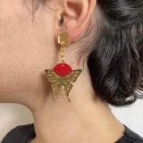 Par de aros colgantes con forma de mariposa plateada con detalles en negro y círculo superior rosa.