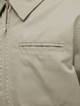 Campera tipo worker de color beige, con cuello camisero, cierre frontal completo y bolsillos laterales. Presenta un diseño minimalista y funcional con acabado limpio.