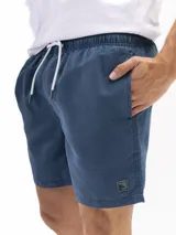 Short de baño de microfibra color azul oscuro, con cintura elástica y cordón de ajuste blanco. Presenta bolsillos laterales y un bolsillo trasero con tapa. Incluye un pequeño parche cuadrado con logo en la parte inferior delantera.