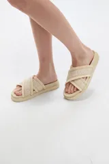 Sandalias planas color crudo con tiras cruzadas de tejido textil con diseño geométrico y detalles de flecos en los bordes.