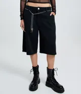 Bermuda tipo jorts de tiro bajo, confeccionada en denim de algodón. Presenta un corte recto y estructurado, con bolsillos funcionales, trabillas en la cintura y un cinturón decorativo de cadena metálica.