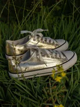 Zapatillas deportivas plateadas con cordones blancos y suela blanca con línea negra.