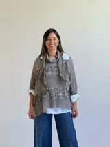 Sweater de punto color visón con diseño superpuesto, que incluye una bufanda integrada y detalles de encaje floral en el frente. Presenta mangas tres cuartos con puños abotonados y un corte holgado.