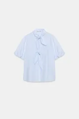 Blusa a rayas celestes y blancas, de manga corta abullonada, con cuello adornado con lazos y cierre frontal con botones.