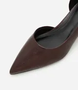 Zapato tipo scarpin con tacón kitten heel, confeccionado en poliuretano con textura símil cuero. Presenta punta fina y un diseño con recorte asimétrico en el empeine.