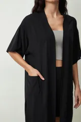 Camisa negra de manga corta, estilo kimono o bata ligera, con cuello solapa y bolsillos frontales amplios.