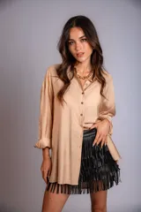 Camisa beige de corte holgado, con cuello camisero, cierre frontal con botones y mangas largas con puños abotonados.