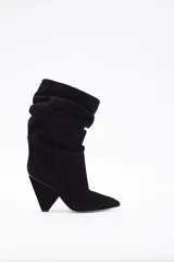 Botín de caña media en gamuza negra, con diseño slouchy y taco cónico de altura media. Presenta punta fina y una estructura flexible en la parte superior de la caña.