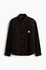 Camisa oversized de pana de algodón color marrón oscuro, con cuello inglés, cierre de botones a presión, dos bolsillos de parche en el pecho (uno con aplique), mangas largas con puños abotonados y bajo redondeado.