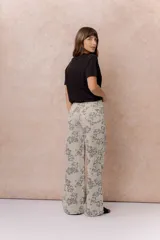 Jean wide leg de tiro alto con estampado floral integral en tonos grises sobre base beige. Cuenta con cierre frontal con botón, pasacintos y bolsillos funcionales delanteros y traseros.