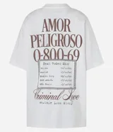 Remera oversized de algodón color crudo, con cuello redondo y mangas cortas. Estampa trasera con texto "Amor Peligroso" y listado de ciudades con fechas, en tipografía estilo western.