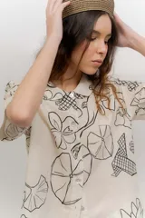 Vestido corto beige con estampado botánico en negro, cuello camisero, mangas cortas y cierre frontal con botones.