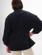 Trench azul marino con cuello alto, cierre frontal de botones a presión y cordón ajustable en la cintura. Presenta cuatro bolsillos frontales con solapa y un parche con el logo de la marca en el pecho.