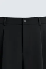 Pantalón de corte relajado en color verde militar, con diseño de pliegues frontales, bolsillos laterales y cierre de cremallera con botón.