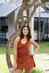 Vestido corto color fucsia con escote en V, breteles finos que se atan al cuello, corte a la altura de la cadera y falda acampanada con ruedo irregular.