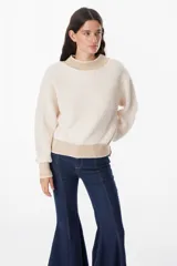 Sweater de punto grueso con diseño bicolor, cuerpo en color crema y detalles en color beige en cuello, puños y ruedo. Presenta mangas largas con caída relajada y cuello redondo.