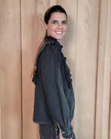 Camisa de denim negro con cuello alto, cierre frontal de botones y detalles de volados en el frente y puños.