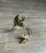 Brazalete rígido abierto de metal plateado con diseño de hojas texturizadas en los extremos.