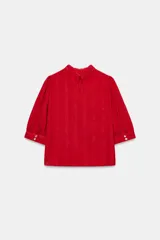 Blusa blanca de cuello alto con detalles de puntilla, manga corta abullonada y cierre posterior con botón.
