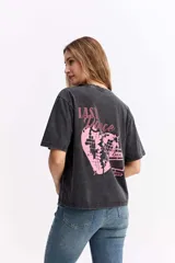 Remera de corte oversize con efecto acid wash en color gris oscuro. Presenta una estampa gráfica en la espalda con la frase 'Last Dance' y un corazón fragmentado en tonos rosados.
