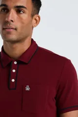 Chomba de piqué color bordó con cuello y puños con detalle de ribete en contraste. Presenta cierre frontal de tres botones y un bolsillo en el pecho con el logo de la marca bordado.