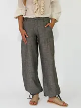 Pantalón de lino color beige, de corte holgado tipo jogger con puños ajustables con cintas en los tobillos, bolsillos laterales y cierre frontal con botón y cremallera.