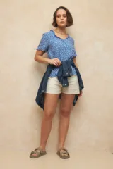 Blusa blanca con finas rayas verticales negras, de manga corta con volados y escote en V con pequeños botones y detalle de volado en el borde.