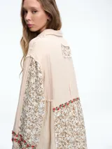Camisa larga de diseño patchwork con cierre frontal de botones, confeccionada en una combinación de texturas lisas y estampados florales con detalles bordados en el canesú y los puños.